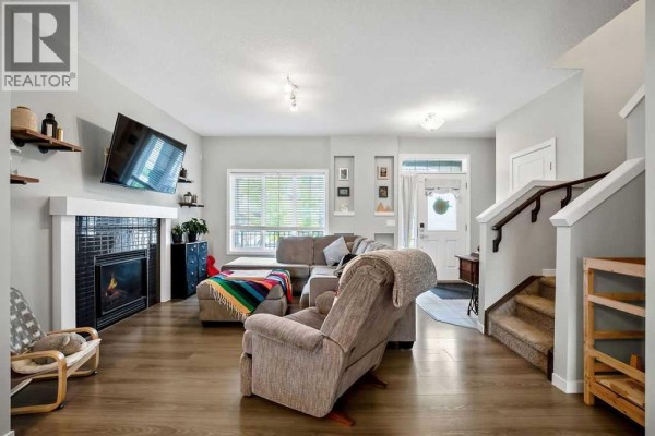 Living room with a fireplace, TV, sectional sofa, armchair, and wood flooring. - 23 Drake Landing Boulevard, Okotoks