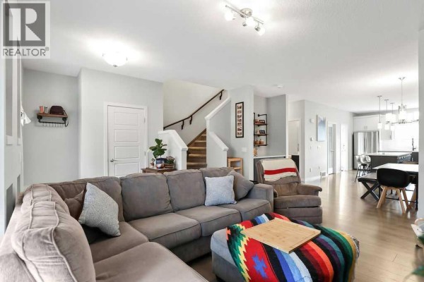 Open-concept living area with large sectional sofa, staircase, and view into the kitchen. - 23 Drake Landing Boulevard, Okotoks