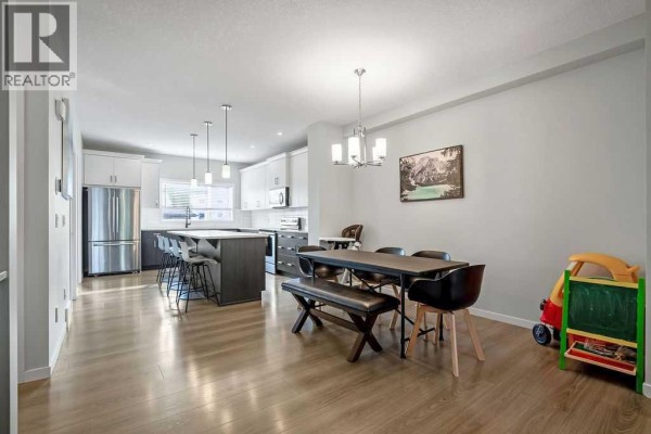 Dining area with table and bench, leading to a modern kitchen with island. - 23 Drake Landing Boulevard, Okotoks