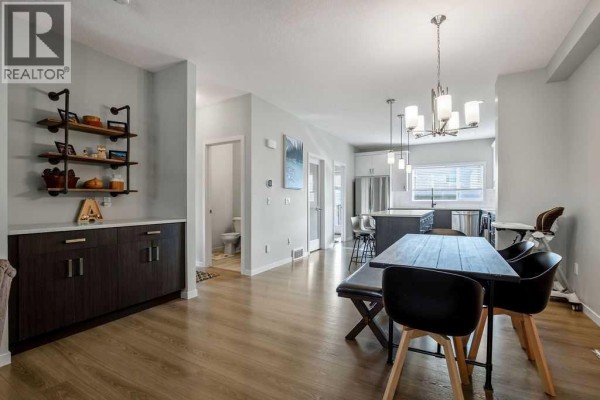 Dining and kitchen area with dark wood cabinets, island, and hallway to a powder room. - 23 Drake Landing Boulevard, Okotoks