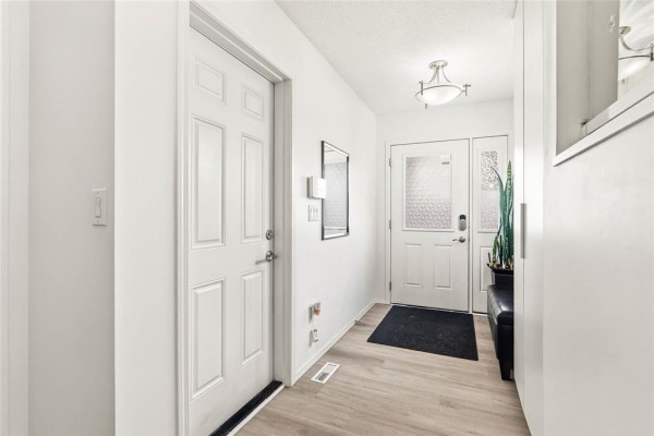 Interior view of a bright white entryway with two doors, laminate flooring, and a black bench. - 23 Driftwater Trail, Winnipeg