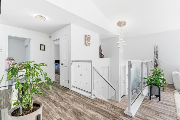 Hallway overlooking a staircase with glass railing, featuring plants and doorways on the left. - 23 Driftwater Trail, Winnipeg