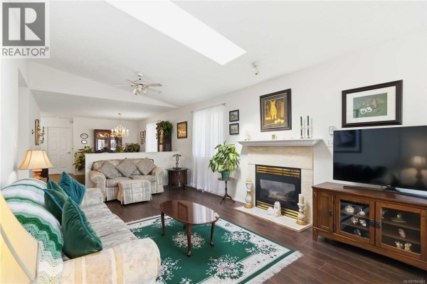 Living room with gas fireplace, beige sofas, dark wood entertainment unit, and skylight. - 23 Eagle Lane, View Royal