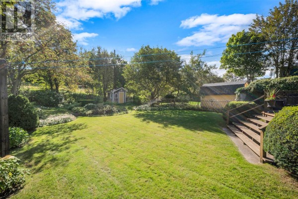 View of a large green lawn with trees, shrubs, a small shed, and a wooden deck. - 23 Long Pond Road, St  John S
