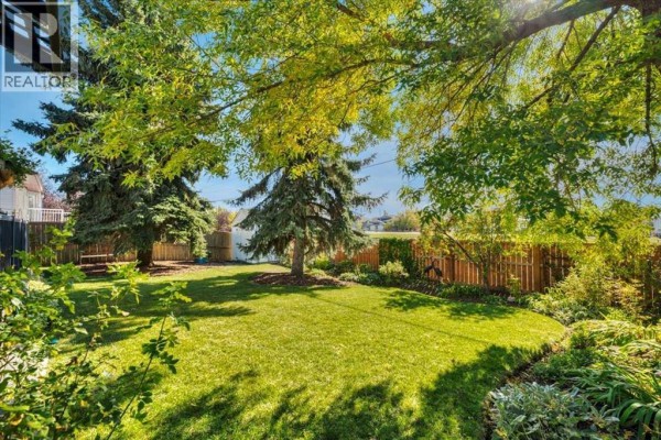 A lush green backyard with mature trees, a wooden fence, and a grassy lawn. - 23 Madison Court, Strathmore