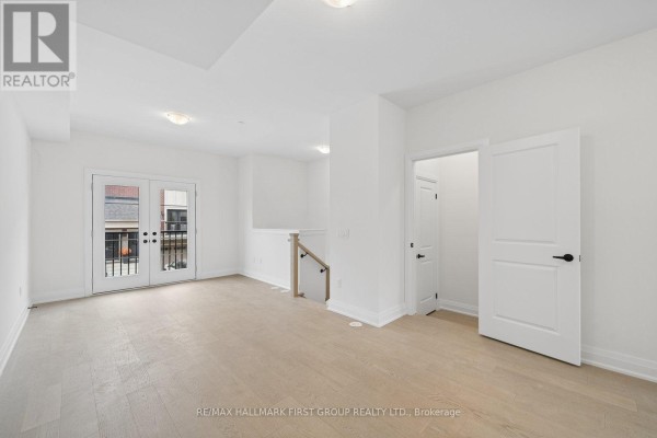 Bright living room with hardwood floors and glass double doors opening to a balcony. - 23 Marret Lane, Clarington
