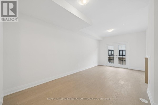Empty living space with hardwood floors and french doors leading to a balcony. - 23 Marret Lane, Clarington