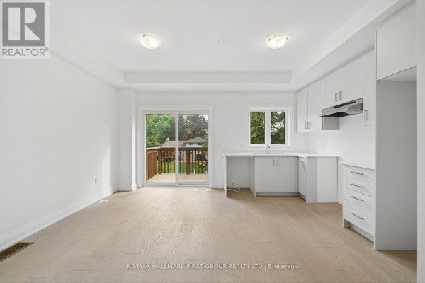 Open-concept living area with white kitchen cabinets, sink, window, and sliding glass door. - 23 Marret Lane, Clarington