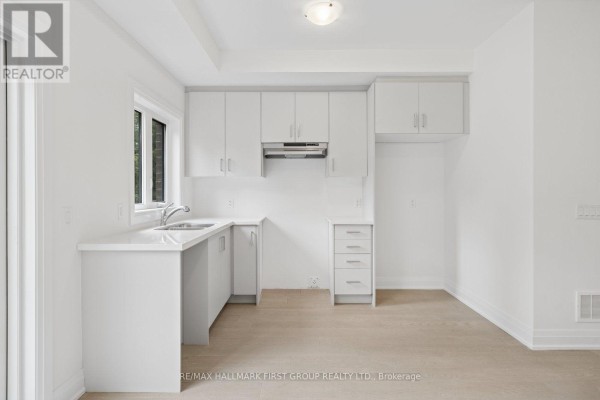 Modern white kitchen with stainless steel range hood, sink, and ample cabinet space. - 23 Marret Lane, Clarington