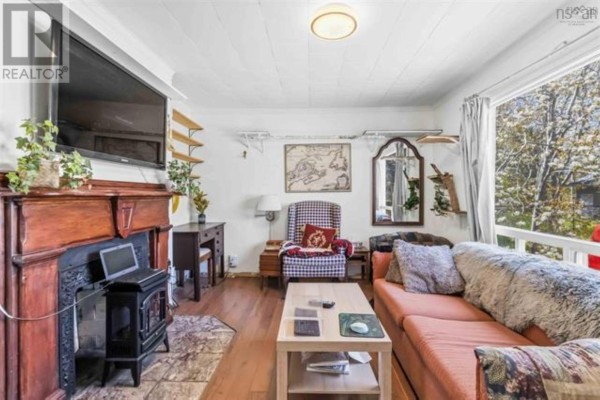 Living room with a fireplace, salmon sofa, armchair, and a window overlooking trees. - 23 Military Road, Halifax