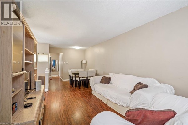 Living and dining area with wood floors, white sofas, and a dining table. - 23 Palomino Drive, Brantford