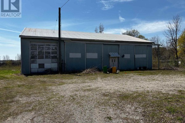 Exterior of a long, industrial building with corrugated metal siding, a large roll-up door, and a small utility structure. - 23 Petrolia Street, Guelph