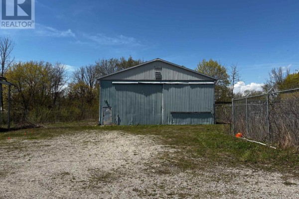 Another view of the corrugated metal industrial building showing its side entrance, roll-up door, and surrounding chain-link fence. - 23 Petrolia Street, Guelph