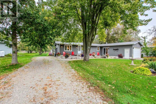 View of the grey bungalow from the driveway, showing the house, garage, and surrounding trees. - 23 Poplar Crescent, Ramara