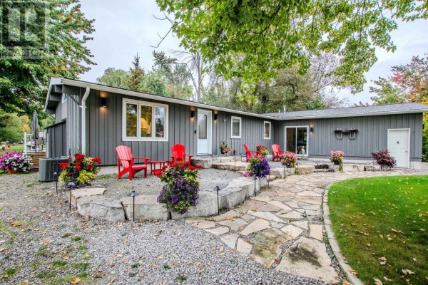 Rear exterior of the grey bungalow with a stone patio, flagstone walkway, and red Adirondack chairs. - 23 Poplar Crescent, Ramara