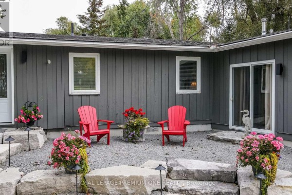 Close-up of the grey bungalow's backyard patio with two red chairs, stone landscaping, and flowering plants. - 23 Poplar Crescent, Ramara