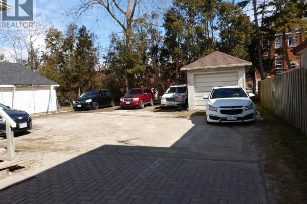 Parking area with multiple vehicles and a detached garage surrounded by trees. - 23 Queeens Avenue, Leamington
