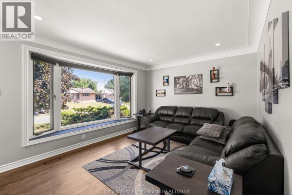 Living room with large bay window, black leather sectional, and dark wood coffee tables. - 23 Queensway Drive, Chatham