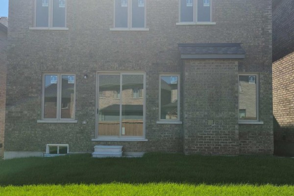 Rear exterior brick wall of a house with a sliding glass door and multiple windows. - 23 Rogerson Street, Clarington