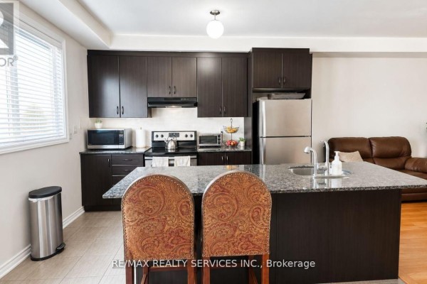Kitchen with dark wood cabinets, granite countertops, stainless steel appliances, and an island with seating. - 23 Sail Road, Brampton