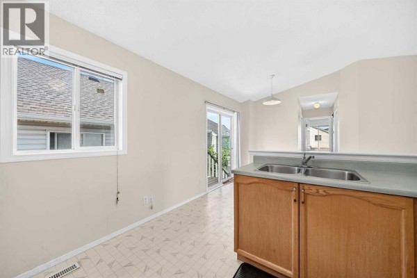 Kitchen area with window, sliding glass door, and wooden cabinets. - 23 San Diego Manor Ne, Calgary