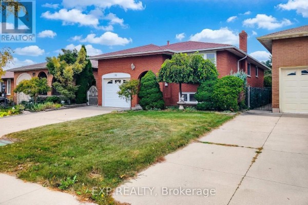 Side exterior view of the red brick house with a driveway and lawn, showing the garage and arched entry. - 23 Tara Court, Hamilton