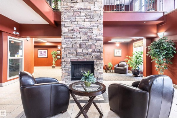 Seating area with two leather chairs, a round glass-top table, and a stone fireplace. - #230 45 Inglewood Dr, St  Albert