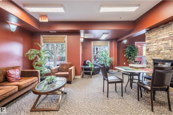 Community room with brown sofa, armchairs, table and chairs, and a stone fireplace feature. - #230 45 Inglewood Dr, St  Albert