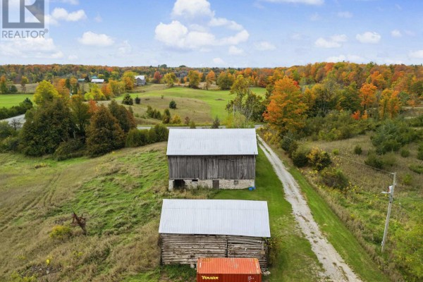 Two wooden barns with metal roofs sit side-by-side on a grassy field, with a dirt road. - 230 Baker Road, Havelock Belmont Methuen