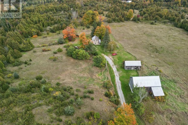 Aerial view of a property with a house, two barns, and a winding dirt driveway through trees. - 230 Baker Road, Havelock Belmont Methuen