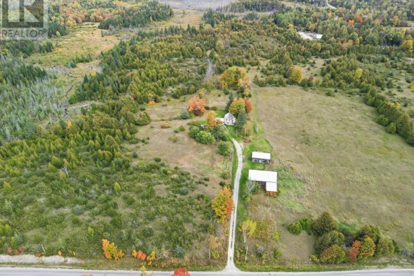 Expansive aerial view of a rural property featuring a house, barns, and surrounding woodland in fall. - 230 Baker Road, Havelock Belmont Methuen