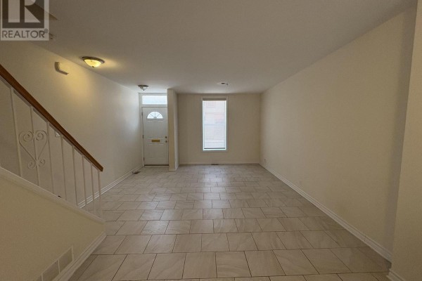 Living room with beige walls, tile floor, and staircase on the left. - 230 Cumberland Street, Ottawa