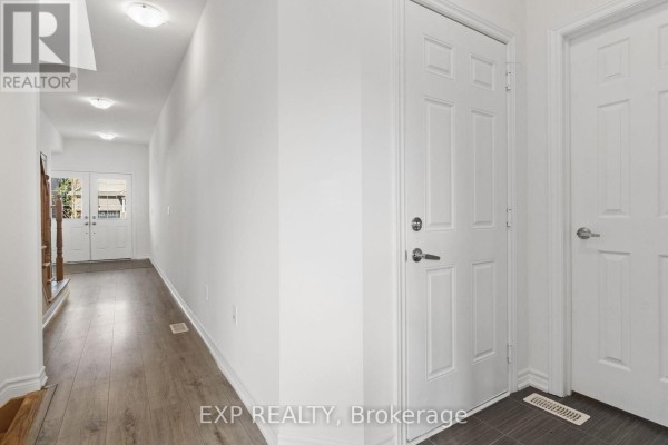 Wide hallway with white walls, doors, and light wood laminate flooring leading to the entrance. - 230 Ridley Crescent, Southgate