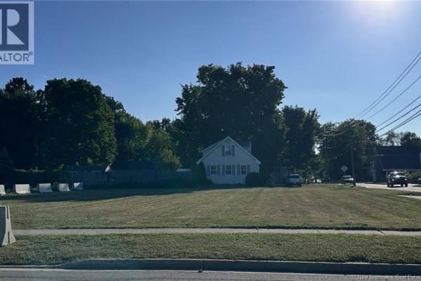 Side view of a cream colored bungalow with green trees and foliage surrounding it. - 230 Woodstock Road, Fredericton