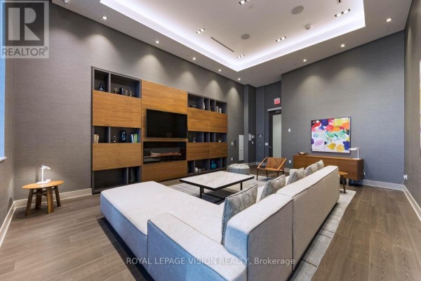 A large sectional sofa faces a media unit in a grey common room. - 2301 - 10 York Street, Toronto
