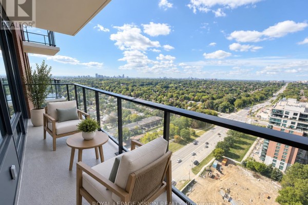 Balcony with two chairs and a small table, overlooking a city skyline and parkland. - 2301 - 4010 Eglinton Avenue W, Toronto