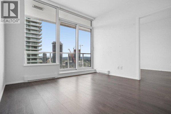 Living room with dark hardwood floors and a large window with city and mountain views. - 2301 1955 Alpha Way, Burnaby