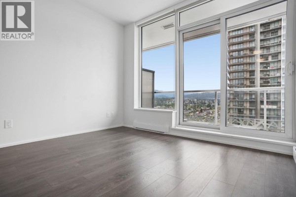 Bedroom with dark hardwood floors and a floor-to-ceiling window overlooking the city. - 2301 1955 Alpha Way, Burnaby