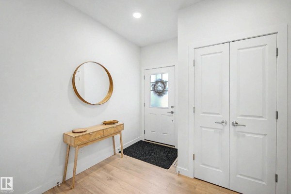 Interior foyer with white walls, light wood floors, a round mirror, and a console table. - 23015 96 Av Nw, Edmonton