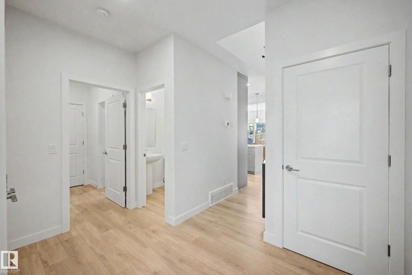 Interior hallway with white walls, light wood floors, and doors leading to different rooms. - 23015 96 Av Nw, Edmonton