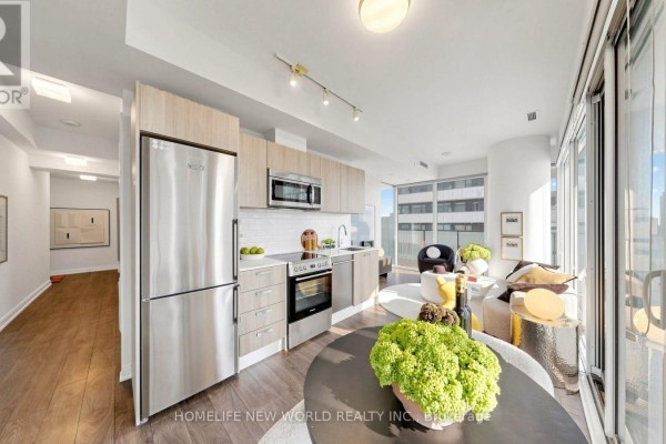 Open concept kitchen and living area with stainless steel appliances and hardwood floors. - 2302 - 42 Charles Street E, Toronto