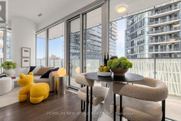 Living area with a sofa, armchair, and large windows with a view of modern buildings. - 2302 - 42 Charles Street E, Toronto