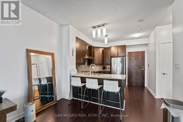 Open concept living area with a kitchen island, bar stools, dark floors, and a large mirror. - 2304 - 18 Harbour Street, Toronto