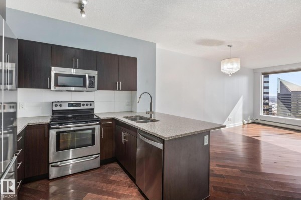 Modern kitchen with dark cabinets, stainless steel appliances, granite countertops, and open living area. - #2304 10152 104 St Nw, Edmonton
