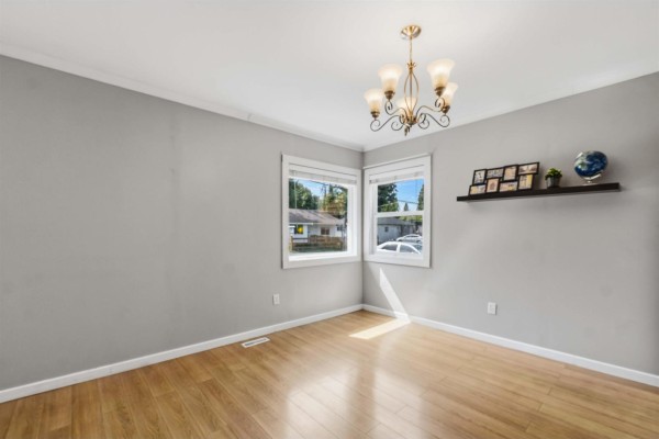 Dining area with light wood floors, gray walls, two windows, a chandelier, and a shelf with photos. - 2304 Mouldstade Road, Abbotsford