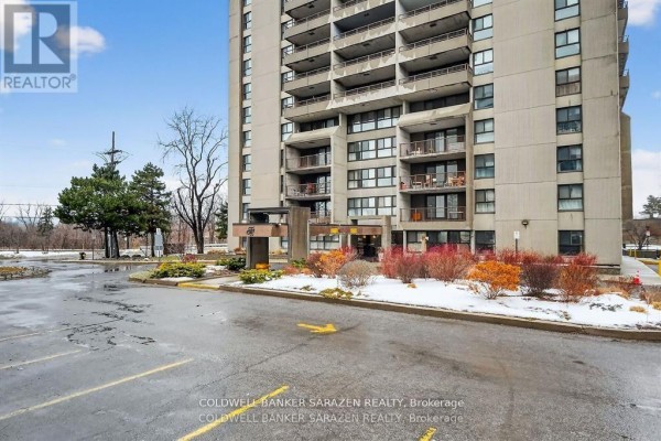 Ground-level view of the building entrance and parking area with snow on the ground. - #2305 - 1785 Frobisher Lane, Ottawa