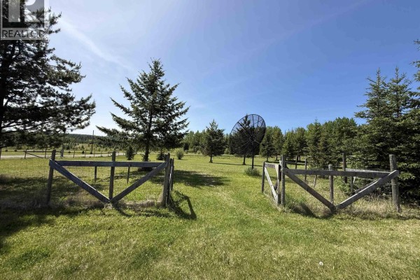 Wooden gate entry to a grassy field with mature trees and large satellite dishes. - 2305 Murray Road, Quesnel