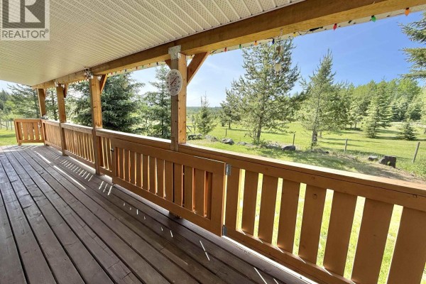 Wooden deck porch with railings overlooking a green landscape and distant hills. - 2305 Murray Road, Quesnel