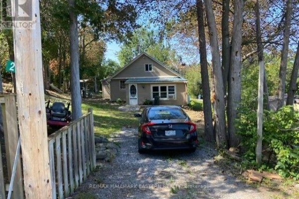 Side view of a beige cottage with a light blue metal roof and surrounding trees. - 2305 Thurstonia Road, Kawartha Lakes