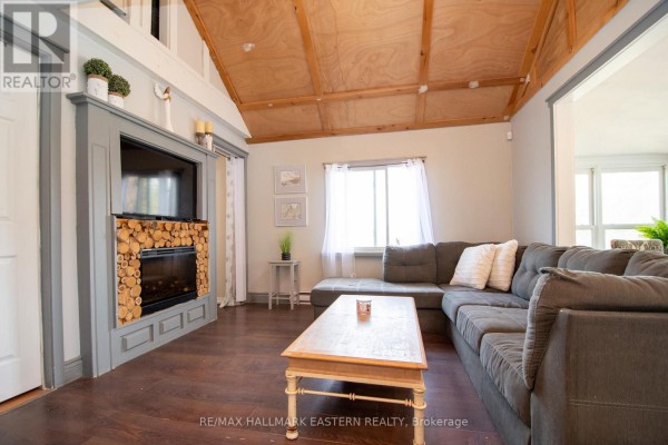 Living room with a large sectional sofa, a fireplace with log accents, and a wood ceiling. - 2305 Thurstonia Road, Kawartha Lakes